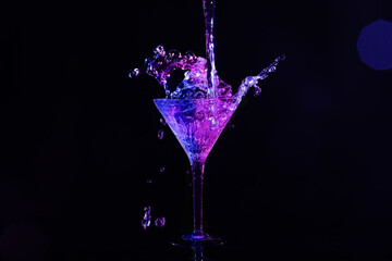 Pouring martini. Glass and splashes in neon lights on dark background, bokeh effect