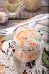 Glass jar of tasty sauerkraut and ingredients on wooden table