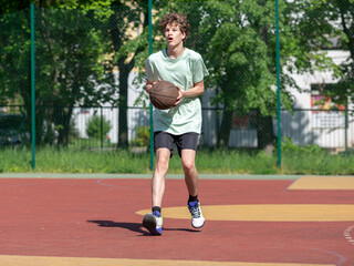 Teenager running in the stadium. Cute young teenager in t shirt with a ball plays basketball on court. Sports, hobby, active lifestyle for boys	