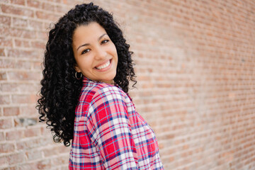 Fototapeta na wymiar young latina woman, exchange student with curls looks at camera, brick background, copy space
