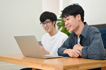 Obraz premium Two of smart young Asian male college students looking at laptop screen. side view