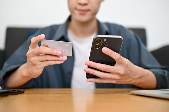 cropped image, A handsome Asian man sits at the table holding a credit card and a smartphone.