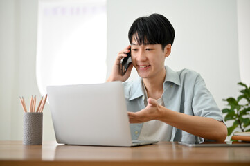 Fototapeta premium Handsome Asian man on the phone with his coworker, explaining something over the call