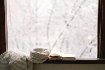 Cozy winter still life. Cup of hot tea and an open book with a warm sweater on a vintage wooden...