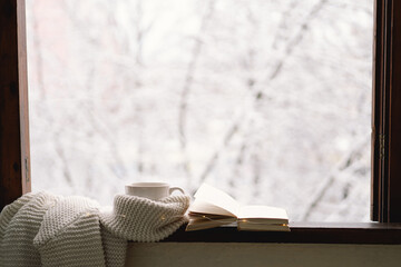 Cozy winter still life. Cup of hot tea and an open book with a warm sweater on a vintage wooden...