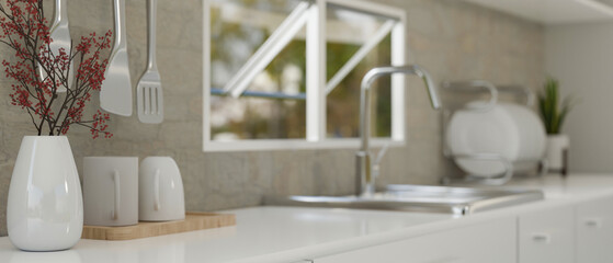 Modern white kitchen counter against the grey wall with window, sink and kitchenware