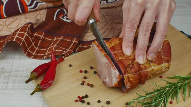 Cutting slices of juicy pork ham on a wooden cutting board with a carving knife. Close-up female hands cutting slices of juicy and tasty pork ham. The concept of cooking delicious meat products