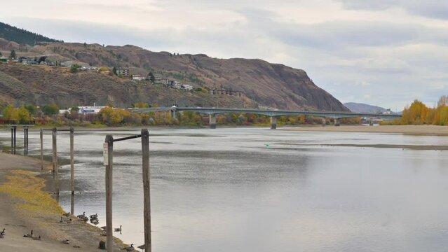 During a cloudy fall day in downtown Kamloops, a panoramic view overlooks the Thompson River with cars driving on the Overlanders Bridge in the distance
