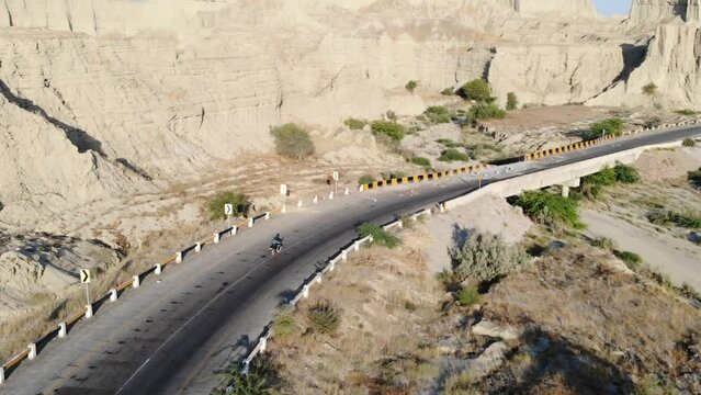 Aerial Tracking Shot Behind Motorbike Driving Along Empty Curved Highway Road Through Hingol National Park In Balochistan Desert Landscape.
