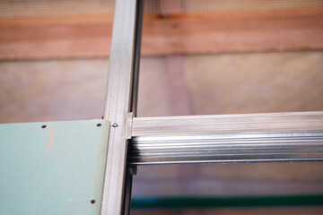 The beginning of the process of sheathing the frame with drywall. One sheet of moisture-resistant drywall is screwed to a metal profile in a close-up on a blurred background, bottom view