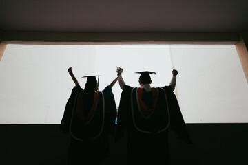 Silhouette of two graduates holding up hands celebrating success.