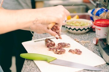 Young, latina, hispanic woman chopping salami on the kitchen counter with a bowl full of guacamole in the background.