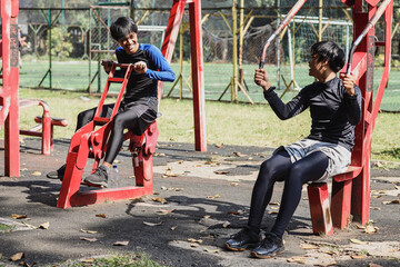 Two young Asian man wearing sportswear exercising and conversing at outdoor park gym open air...