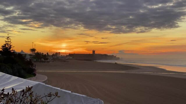 Lonely trator working on beach with lights on with dramatic sunset on the empty beach in background, marginal road, Carcavelos