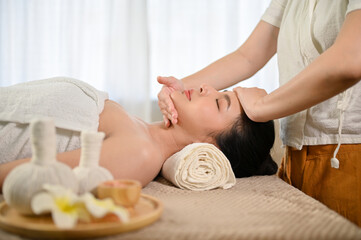 Obraz na płótnie Canvas side view, Attractive Asian woman eyes closed, receiving facial massage treatment at spa salon.