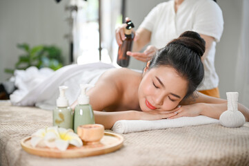 Obraz na płótnie Canvas Relaxed Asian woman lying on massage table, receiving body massage, enjoying Thai spa at salon.