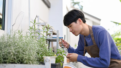 Handsome Asian man watering his organic plants in the backyard. Home gardening concept.