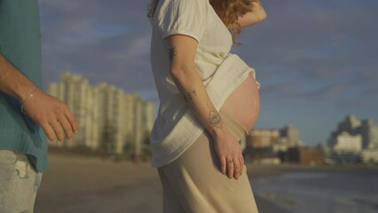 Lovely pregnant couple at the Beach in Uruguay. Father kissing belly front to ocean and redhead mother smiles. - Powered by Adobe