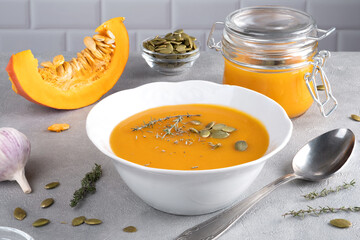 Pumpkin puree soup with pumpkin seeds and thyme in a white plate and glass jar. Healthy diet....