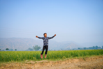 Fototapeta premium Indian little boy spreading hand and jumping at agriculture field.