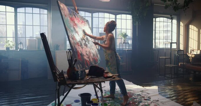 A woman in a dark workshop draws an abstract picture with her hands on a large and huge canvas. Woman artist creates art with her hands, making finishing touches, completing picture. Creation of art.