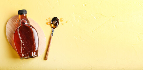 Bottle and spoon of maple syrup on light yellow background with space for text