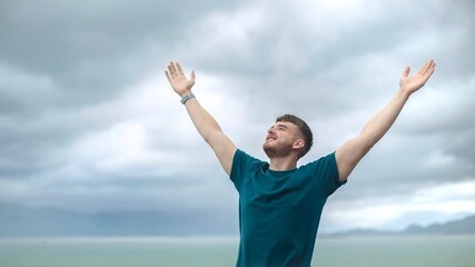 happy handsome free guy, young calm relaxed carefree man traveler with open raised hands enjoy sea, ocean view, person feeling good, breath deep deeply fresh air. Freedom, travel, happiness concept - obrazy, fototapety, plakaty