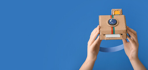 Female hands with cardboard photo camera on blue background with space for text