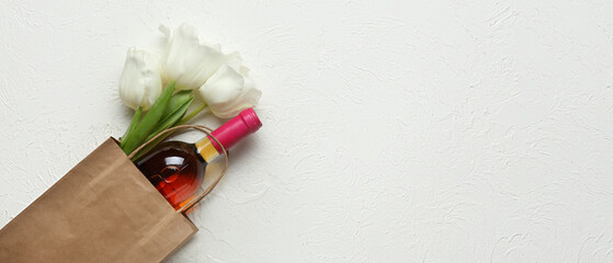 Bag with bottle of wine and flowers on white background with space for text