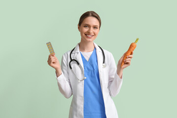 Female doctor with vitamins and carrot on green background