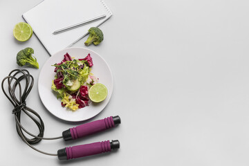 Plate with vegetable salad, skipping rope and notebook on grey background
