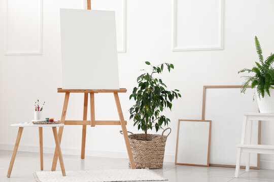Interior of light room with easel, houseplants and blank frames