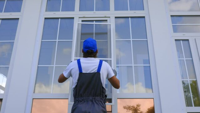 Thumbs up shows the working one after successfully installing a mosquito net on a large window of the house. Man in a work jumpsuit puts a protective net on the window