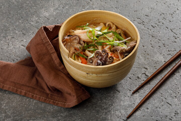 Bowl of soba noodle with sea food, octopus, shrimps served with green onion over grey background. Traditional asian food