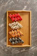 Japanese food. Set of different types of sushi served with soy sauce, wasabi  and chopsticks on wooden plate over grey background. Minimalistic style