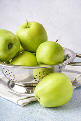 Colander of fresh green apples on light background