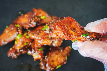 gloved hand and fried chicken with garlic and sesame in caramel on a black tray.