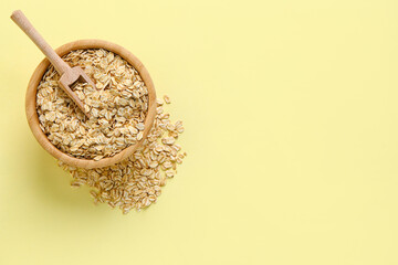 Wooden bowl of raw oatmeal on yellow background