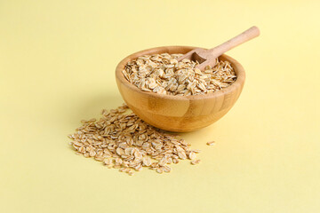 Wooden bowl of raw oatmeal on yellow background