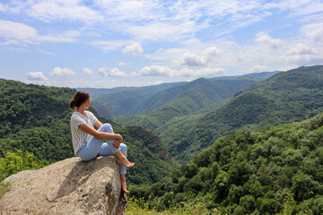 woman sitting on the rock with beautiful green mountains and blue sky on background