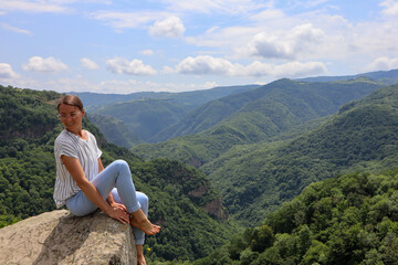 Naklejka na ściany i meble woman sitting on the rock with beautiful green mountains and blue sky on background