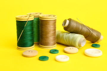Thread spools with needles and buttons on yellow background