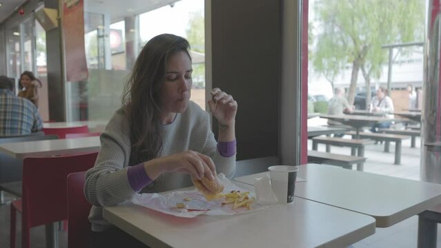 Mujer comiendo hamburguesa en restaurante comida r&aacute;pida (Formato LOG para edici&oacute;n y correcci&oacute;n de color profesional)	