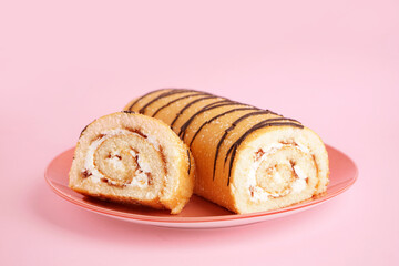 Plate with sweet sponge cake roll on pink background