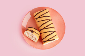 Plate with sweet sponge cake roll on pink background
