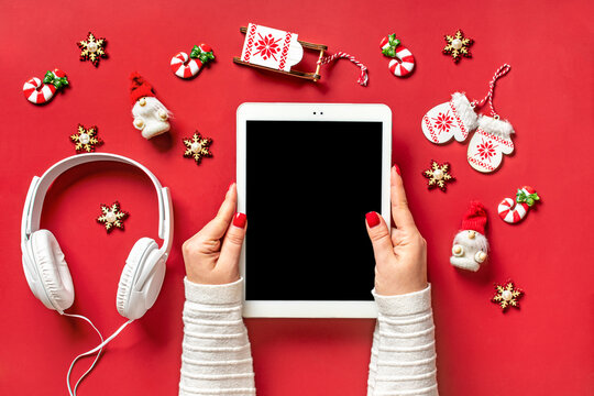 top view female hands holding tablet with black digital screen, Christmas decor, headphones on red table Flat lay Greeting electronic card, book, podcast, music Merry Christmas and Happy New Year
