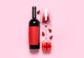 Bottle of wine with glass, Christmas balls and gift on pink background