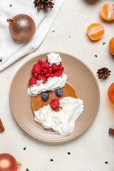 Plate with tasty Santa pancake and Christmas decor on light background