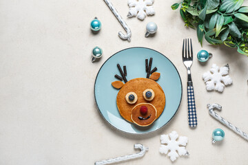 Plate with tasty reindeer pancakes and Christmas decorations on light background