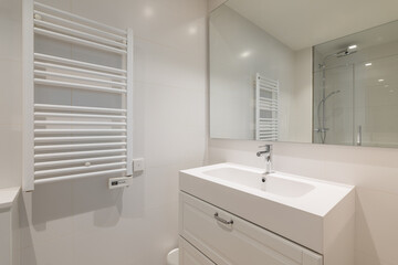 Spacious bright bathroom with a washbasin built into bathroom vanity, a large mirror reflecting the shower on the opposite side of the room, a ceiling and a heating radiator for drying towels.